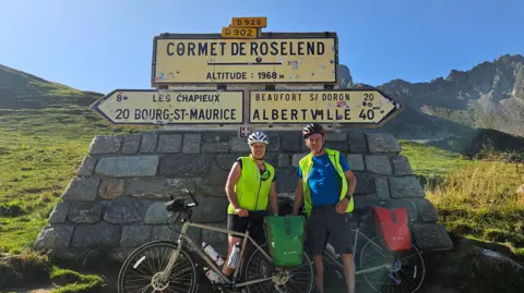 Supplied Richard and Ange Bebbington stood with their bikes in front of a sign during their Rome 2 Home challenge