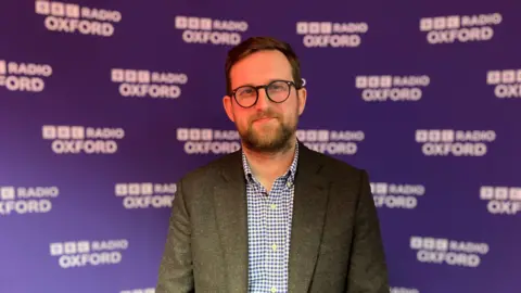 BBC Henley & Thame MP Freddie Van Mierlo stands in front of a purple banner with BBC Radio Oxford branding. 