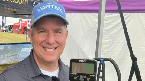 Steve looks into the camera while hold a metal detector