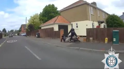 Wiltshire Police A still from a police video of two people falling to the ground from an e-bike after crashing into a wall in a residential road