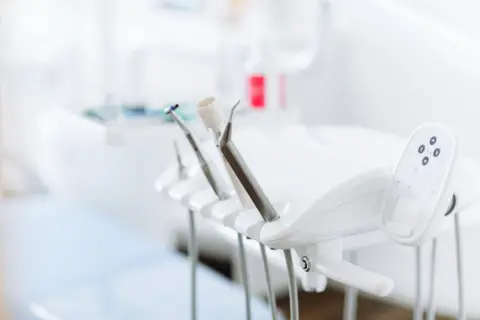 Getty Images A set of dental tools lined up in a holder next to a dentist's chair