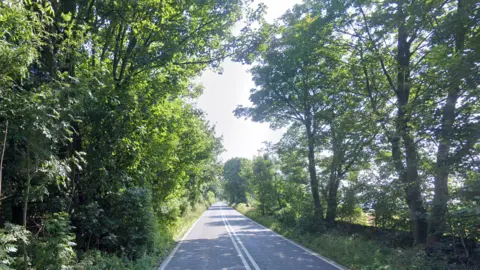 Google A google streetview screengrab of the A436. The two-lane road is narrow and has trees on either side. 