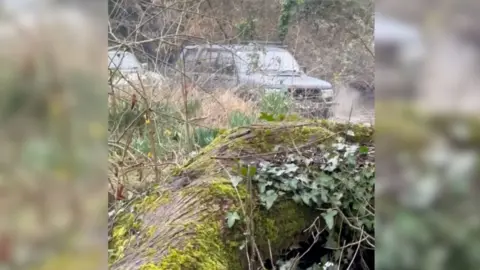 A silver 4x4 is followed by another vehicle along the section of chalk stream open to motor vehicles