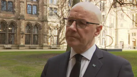 John Swinney wearing a dark suit and looking slightly off camera.