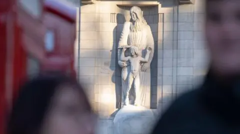 Getty Images The statue in sunlight with the blurred images of passers-by in the foreground. Red telephone boxes can be seen out of focus on the left of the picture