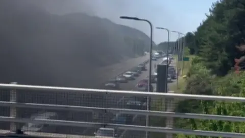 Sam Tibbatts Smoke seen rising from tunnel seen from bridge above and cars stuck in queue