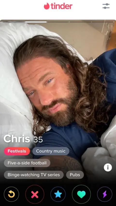 A screenshot of a Tinder profile photo showing Harkins lying on a bed. His right ear is against a white pillow as he looks down towards the camera. He had long dark hair and full beard.