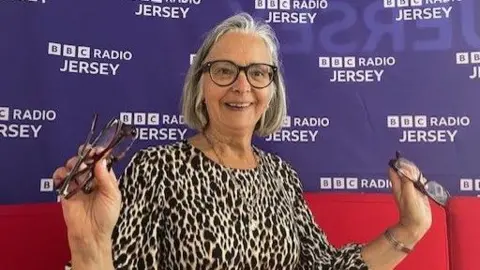 Trena Lewis has a leopard print coloured dress and is sat in front of a BBC Jersey sign. 