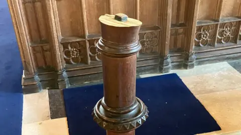 The remains of the wooden lectern with the wooden eagle missing. The top of the lectern is now jagged and broken where the eagle once stood.