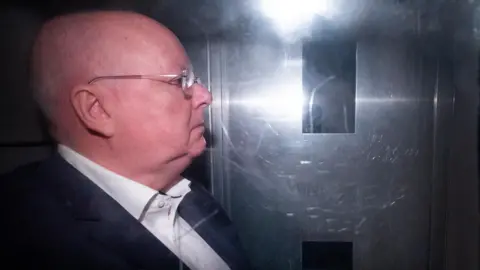 PA Media Peter Murrell inside a prison van. He is shown in profile and is looking to the right of the image. He is wearing a suit jacket, white shirt and glasses.