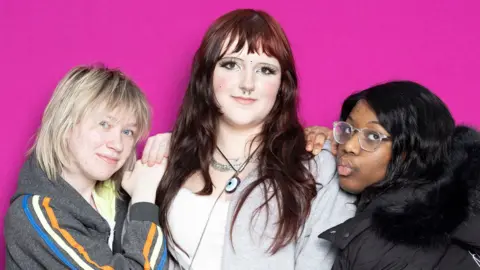 Three young females against a bright pink backdrop