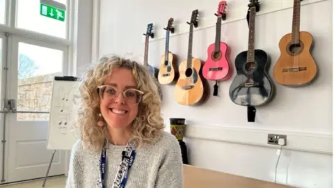 BBC Women smiling in a classroom with guitars behind her.