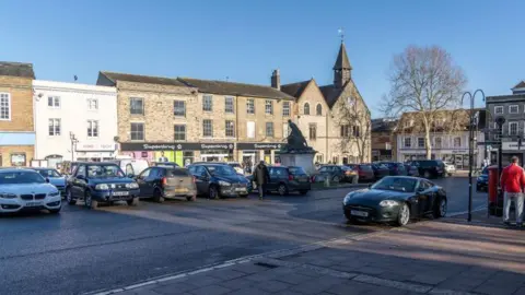 Cars parked on the Buttermarket in Bury St Edmunds with brick buildings behind