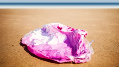 Getty Images A deflated pink inflatable on the sand at the beach, with the sea in the background