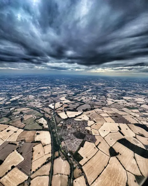 BBC Weather Watchers/Penguin Leader A drone shot of a swathe of fields under a dark, cloudy sky.