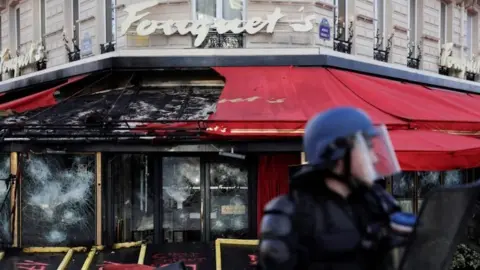 AFP/Getty Images A French riot police officer stands in front of the gutted Le Fouquet's restaurant in Paris. Photo: 16 March 2019