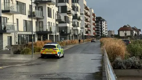 A police vehicle sits on a road in front of apartment blocks.