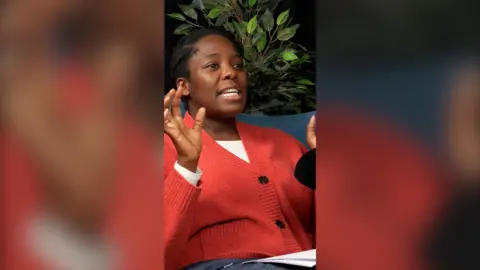 Woman in a red cardigan raising her hands whilst talking