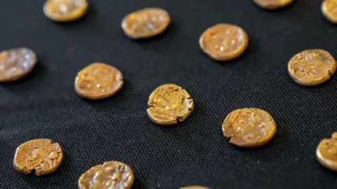 Fountain Media Rows of gold Iron Ag coins lying on black cloth background.