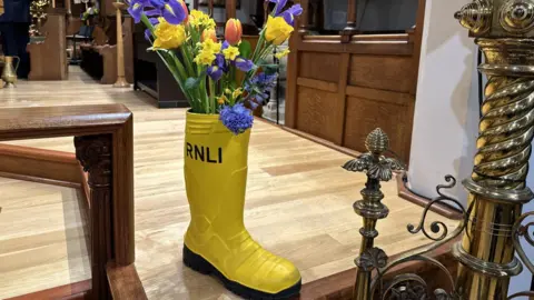 A yellow wellington boot with RNLI written on it holding colourful flowers.