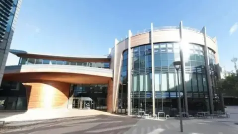 The entrance to one of Durham University's buildings. It is glass fronted with wood panelling. The section to the right is curved.