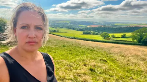 Cheryl Cottle-Hunkin, Devon County Council member, in a black top with views of fields in the background