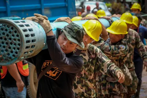 Getty Images Rescue workers carry heavy water pumping equipment into Tham Luang Nang Non cave