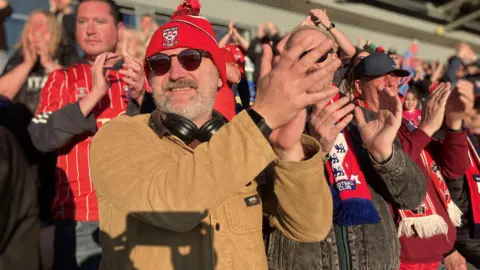 A group of men in red hats, shirts and scarves clap and smile