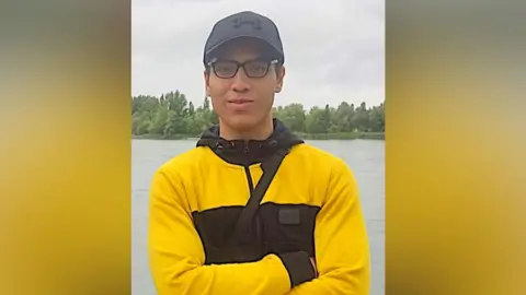 Facebook Nicholas Prosper dressed in glasses, a black baseball hat and yellow and black hoodie