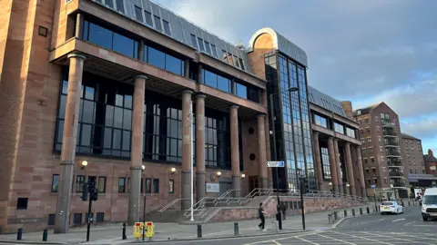 Newcastle Crown Court. It is a large imposing building made from red stones with columns and large dark windows
