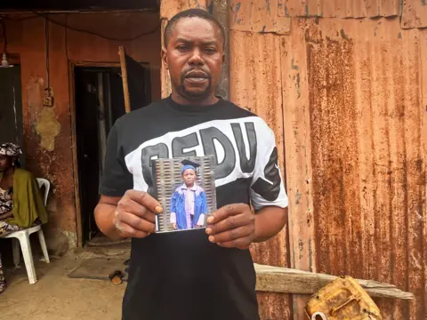 Chris Ewokor/ BBC Victor Dennis holds a cherished photo of his son, Emmanuel, who died.