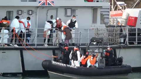 PA Media A group of people, thought to be migrants, disembark the deck of HMC Seeker, as they climb aboard a Border Force rib at Dover marina