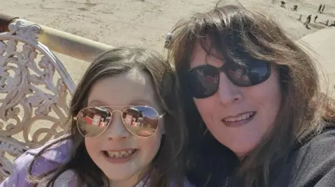 Beatrice and Sandra wearing sunglasses in front of a beach