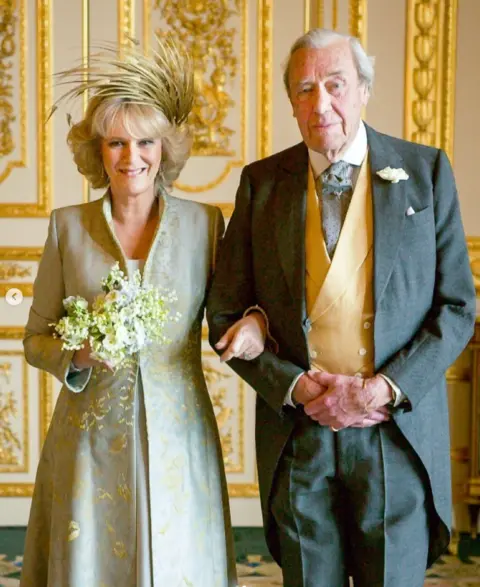 Buckingham Palace A portrait image in colour of Camilla with her father Major Bruce. She has her arm through his and they both look to the camera and smile.