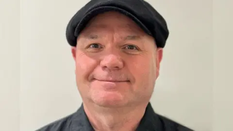 Local Democracy Reporting Service Councillor Mickey Leng wearing a flat cap