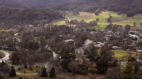 A birds-eye view shows the township of Porepunkah, a cluster of buildings and roads surrounded by green hills and dense bushland