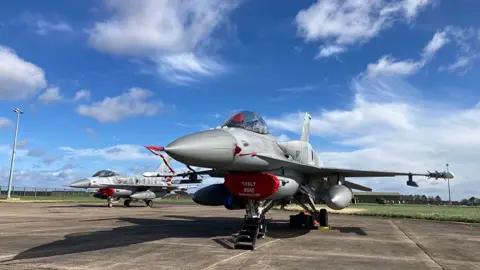 Two Polish F16 fighters painted in grey stand on the tarmac at RAF Waddington