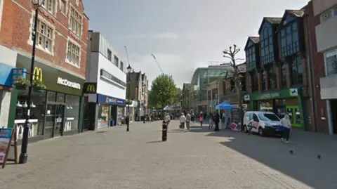 A pedestrianised high street with shops either side including McDonald's and Lloyds Bank.