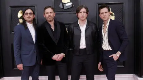Getty Four men who make up the rock band kings of Leon, stood on the red carpet at the Grammy music awards. On the left is Nathan Followill, wearing a Navy suit with a white shirt, he has long below shoulder length hair and is wearing sunglasses. to Nathan's right is Caleb Followill who is wearing an all-black suit. To the right of Caleb is Matthew Followill, he is wearing black trousers, black jacket and a white shirt. To the right of Caleb is Jared Followill, wearing navy trousers and blazer with a striped shirt. 