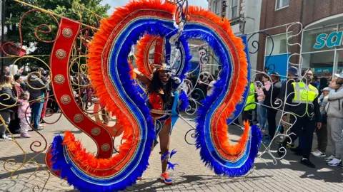 Helen Mulroy/BBC A woman wearing a colourful costume is surrounded by spectators on the street at Luton Carnival.