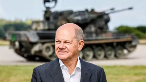 Getty Images Olaf Scholz stands in front of an anti-air defence system