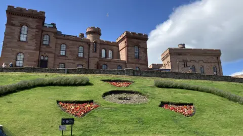 A view towards Inverness Castle and three flower beds and a circle of bare earth where the clock once was.