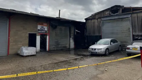 Owen Sennitt/BBC A breezeblock building next to a corrugated iron business unit. They have been blackened and have got holes in them. A sign above a doorway says Sales Office. A yellow fire tape cordon is in front of the buildings.