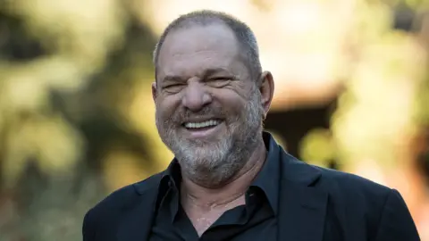 Getty Images Harvey Weinstein, dressed in a dark jacket and shirt, is pictured smiling at the camera in a sunny outdoor setting in 2017