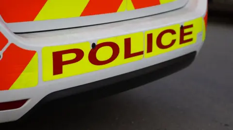 A stock image of a police car's bumper. The word police is picked out in red against a fluorescent yellow and orange background.   