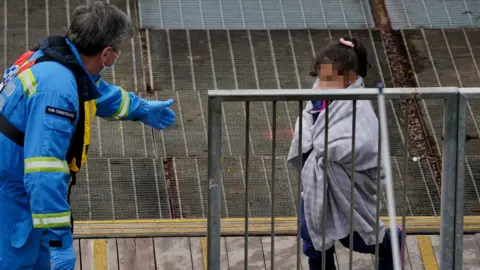 PA Media Child in blanket walks towards coastguard