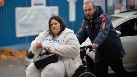 Spindrift Paul Brannan photographed portion    pushing Lesley Williams successful  a wheelchair extracurricular  the High Court successful  Glasgow. Williams has long, acheronian  hairsbreadth  with a mediate  parting and is wearing a achromatic  fleece, achromatic  t-shirt with bluish  writings and achromatic  trousers. She is holding a achromatic  handbag, which is balanced connected  her lap, and is looking consecutive  astatine  the camera with a superior   expression. Brannan is leaning guardant   pushing the wheelchair. He is wearing achromatic  trousers and a navy bluish  Manchester United overgarment   with the nine  crest, adidas logo and 3  stripes connected  the arms successful  red. Brannan has acheronian  thinning hairsbreadth  and a greying beard. He is besides  looking astatine  the camera with a superior   expression.