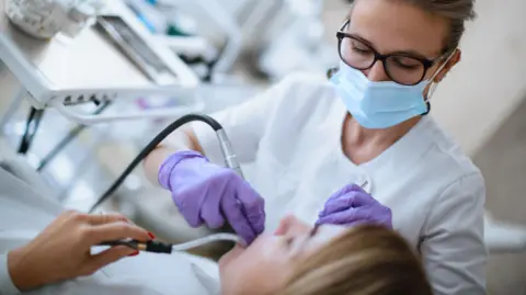 Getty Images Dentist in face mask and purple gloves examining a patient's mouth