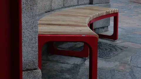 A curved wooden bench, partially painted in red, fits along a curved wall at the market.