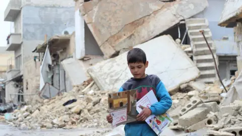 Unicef/Al-Issa A child carries manuals distributed by Unicef volunteers on identifying and reporting unexploded objects in al- Sakhoor neighbourhood of eastern Aleppo, Syria